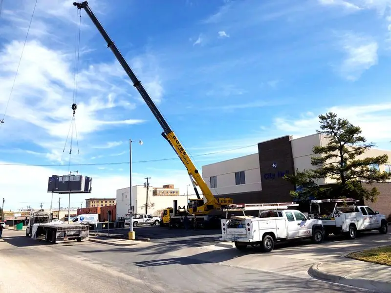 Crane lifting a rooftop unit beside Heart of Texas Mechanical trucks
