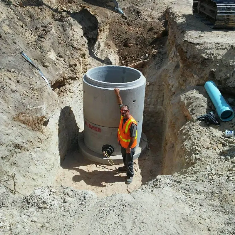 Worker setting a concrete manhole in an excavation