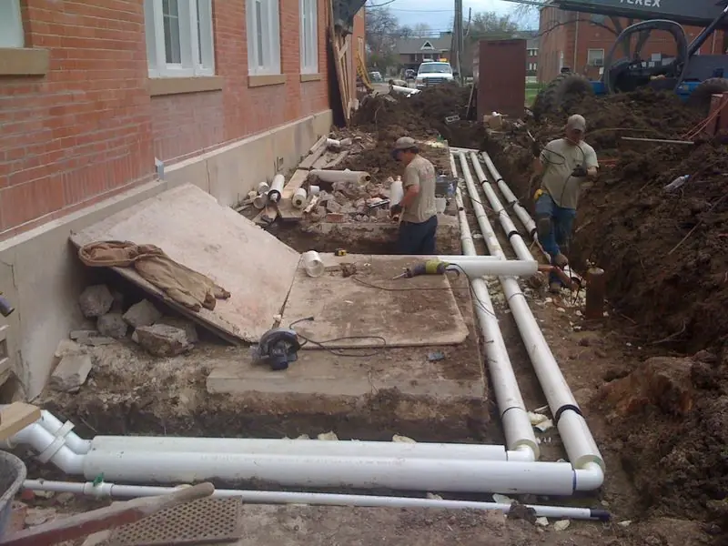 Underground piping being laid beside a brick building
